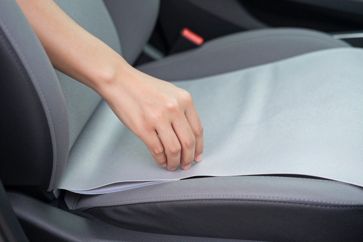 Hand testing car seat tightness over protector mat ensuring less than one inch movement