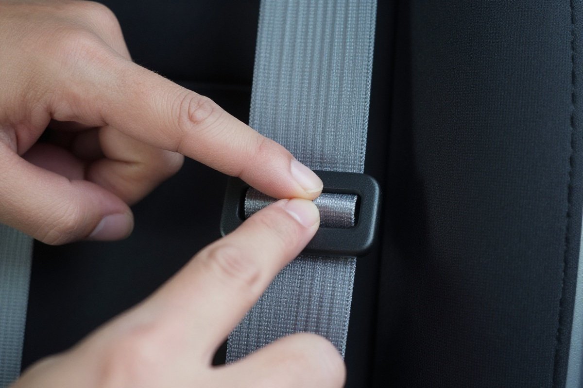 Demonstrating the pinch test on car seat harness strap at shoulder level
