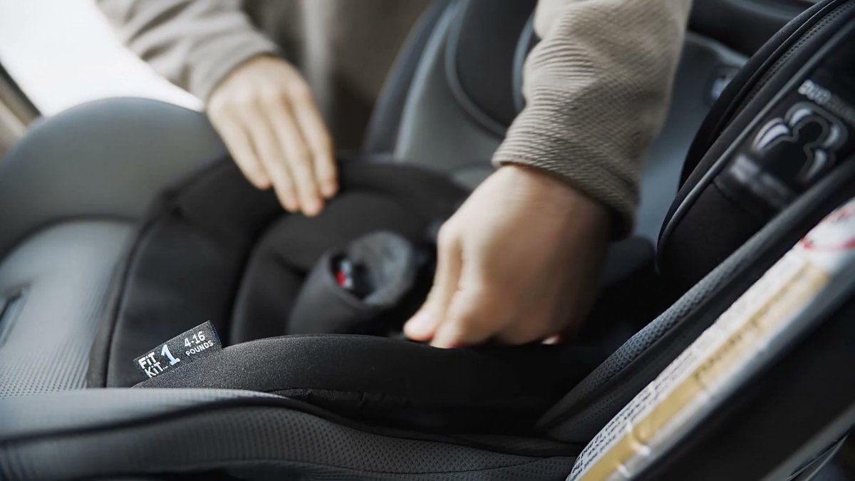 Close-up of hands adjusting harness on Chicco Fit4 car seat, showing Fit Kit 1 label for 4-16 pounds